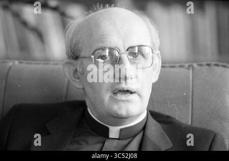 Bischof Bomers of Haarlem, römisch-katholische Kirche, Haarlem, Niederlande, 03-09-1984 Whizgle News, Dutch Desk, Niederlande, 1950-2000 Ein Mann mittleren Alters in einem Anzug mit klerikalem Kragen, mit Brille, scheint tief in Gedanken zu sein, während er sich im Gespräch befindet. Sein Ausdruck deutet auf eine Mischung aus Kontemplation und Sorge hin, wobei ein Hintergrund auf ein wissenschaftliches Umfeld hindeutet. Stockfoto