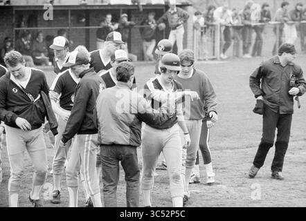 Terrasvogels - Hoofddorp, Baseball Terrasvogels, 05-05-1985 Whizgle News, Dutch Desk, Niederlande, 1950-2000 Eine Gruppe von Baseballspielern in Uniformen wird auf dem Spielfeld beobachtet, wobei einige Trainer und Zuschauer im Hintergrund eine lebhafte Sportatmosphäre schaffen. Die Spieler scheinen ein aktuelles Spiel zu feiern oder zu diskutieren, indem sie Kameradschaft und Teamwork zeigen. Stockfoto
