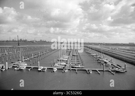 Marina, IJm., IJmuiden, Niederlande, 05-12-1994 Whizgle News, Dutch Desk, Niederlande, 1950-2000 Ein ruhiger Yachthafen verfügt über zahlreiche verankerte Segelboote, die ordentlich an hölzernen Docks angeordnet sind und sich in Richtung einer entfernten Skyline erstrecken, die von Wolken und Industriebauten akzentuiert wird. Stockfoto