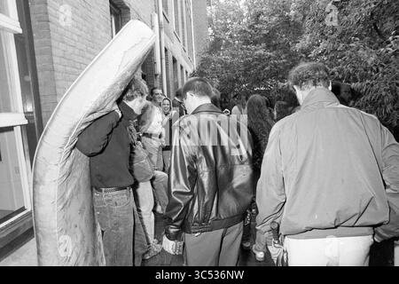 Marinekrankenhaus besetzte, 14-09-1991 Whizgle News, Dutch Desk, Niederlande, 1950-2000 Eine Gruppe von Menschen ist vor einem Gebäude versammelt, wobei eine Person schwer ist, eine große Matratze zu tragen. Andere führen Gespräche und schaffen eine lebendige Atmosphäre, während sie durch den engen Raum navigieren. Die Szene fängt einen Moment der Kameradschaft und Aktivität unter Freunden ein. Stockfoto
