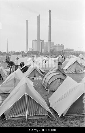 Campingplatz Strand 6-Tage-Wanderer, Velsen Noord, Kampen, Campingplätze, Campingplatz, Camping, Camping Hütte, 23-07-1975 Whizgle News, Dutch Desk, Niederlande, 1950-2000 Eine Gruppe von Menschen baut auf einem großen Feld Zelte auf, in denen industrielle Schornsteine und ein Kraftwerk sichtbar sind. Die Szene fängt eine Mischung aus menschlicher Aktivität und städtischer Infrastruktur ein und kontrastiert Natur und Industrie. Stockfoto