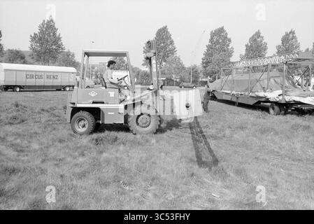 Bau des Zirkus Renz in Schalkwijk, Haarlem, Niederlande, 07-05-1990 Whizgle News, Dutch Desk, Niederlande, 1950-2000 Eine Person bedient ein kleines Baufahrzeug und manövriert es durch eine Grasfläche in der Nähe eines Zirkusaufbaus. In der Nähe sind ein großer Anhänger und teilweise demontierte Maschinen zu sehen, was auf eine geschäftige, aber temporäre Umgebung hindeutet. Stockfoto
