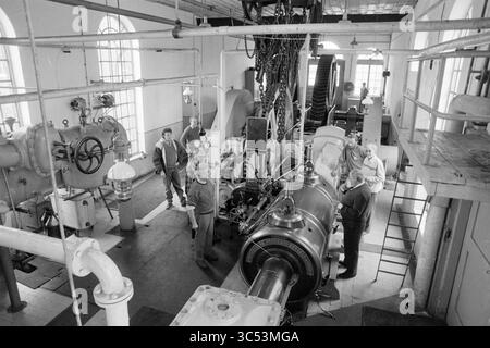 Wiedereröffnung der Dampfpumpenstation auf halbem Wege, Eröffnung, Öffnungen, Inbetriebnahme, Dampfpumpenstation und Dampfpumpenstation, Halfweg, 01-04-1989 Whizgle News, Dutch Desk, Niederlande, 1950-2000 Eine Gruppe von Ingenieuren und Technikern arbeitet in einer großen Industrieanlage zusammen, die von komplexen Maschinen und Rohren umgeben ist. Der Raum ist mit verschiedenen Anlagen gefüllt, darunter eine prominente Turbine oder ein Generator in der Mitte, was die Komplexität der laufenden Vorgänge unterstreicht. Die Atmosphäre deutet auf eine Zusammenarbeit in einem technischen Umfeld hin. Stockfoto