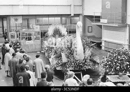 Blumenparade Aalsmeer, Blumenparade, Blumenausstellung, 01-09-1967 Whizgle News, Dutch Desk, Niederlande, 1950-2000 In der Mitte einer belebten Ausstellungshalle steht Ein großer, pfauenförmiger, floraler Wagen, umgeben von Zuschauern, die sein kompliziertes Design bewundern. Farbenfrohe Blumenarrangements und Grün zieren den Wagen, während die Zuschauer Gespräche führen und die lebhafte Atmosphäre der Veranstaltung verstärken. Stockfoto