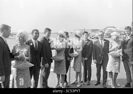 Ankunft des amerikanischen Teams in Schiphol, Baseball, People, 01-07-1966 Whizgle News, Dutch Desk, Niederlande, 1950-2000 Eine Gruppe elegant gekleideter Individuen steht auf einem Flughafen zusammen, einige halten gewebte Körbe und andere verhandeln sich. Zu den Kleidungsstücken gehören Anzüge und stilvolle Kleider, die durch einzigartige Hüte ergänzt werden. Die Atmosphäre deutet auf eine Feier oder einen besonderen Anlass hin, mit einem Flugzeug, das im Hintergrund sichtbar ist. Stockfoto