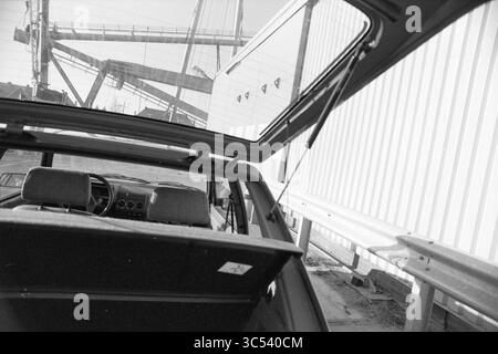 Crane Sparne aus Figee, Figee, 30-11-1989, Whizgle News, Dutch Desk, Niederlande, 1950-2000 Ein Oldtimer mit offener Luke oder offenem Cabrioverdeck, der den Innenraum mit schlichten, klassischen Designs vor dem Hintergrund von Industriestrukturen und einem teilweise sichtbaren Kran freigibt. Die Szene weckt ein Gefühl von Nostalgie und deutet auf eine urbane Umgebung hin. Stockfoto