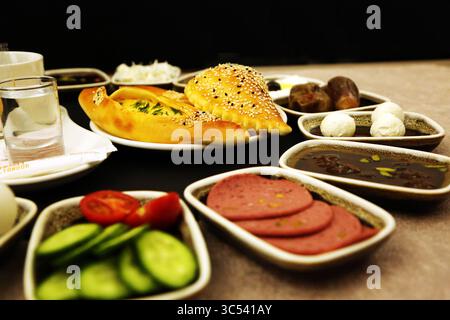 Frühstückstisch aus dem Nahen Osten mit frischem Gemüse, Dattelobst, Labneh-Bällchen in Olivenöl, Melasse-Marmelade und frisch gebackenem Käsegebäck. Stockfoto