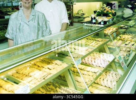 Patisserie Tummers, Heemstede, Heemstede, Binnenweg, Niederlande, 03-08-2000 Whizgle News, Dutch Desk, Niederlande, 1950-2000 Ein freundlicher Bäcker und Assistent steht stolz hinter einer Glasvitrine voller bunter Gebäckstücke und Süßigkeiten, in der verschiedene Kekse, Kuchen und Konfekt präsentiert werden. Die warme Atmosphäre lädt Gäste ein, die köstlichen Leckereien zu erkunden. Stockfoto