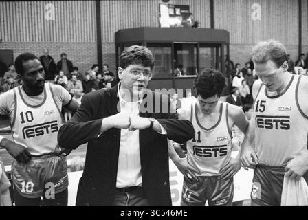 Basketballspiel Whizgle News, Dutch Desk, Niederlande, 1950-2000 Ein Basketballtrainer spricht während einer Auszeit leidenschaftlich an sein Team, wobei zwei Spieler auf beiden Seiten aufmerksam zuhören. Die Atmosphäre ist fokussiert und spiegelt die Intensität des Spiels wider, während der Trainer seine Strategie mit Nachdruck zum Ausdruck bringt. Stockfoto