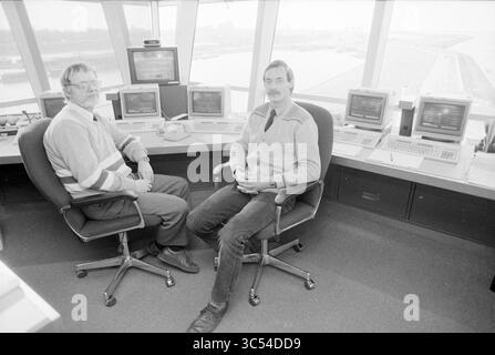 Neue Ausrüstung IJmuiden Port Service, Ports, IJmuiden, Niederlande, 24-02-1987 Whizgle News, Dutch Desk, Niederlande, 1950-2000 zwei Männer sitzen in einem modernen Kontrollraum mit Computermonitoren und Blick auf die Start- und Landebahn des Flughafens. Sie scheinen in Gesprächen zu verwickelt, in lässiger Kleidung, wobei die Arbeitsumgebung eine Reihe von technischen Geräten und Bildschirmen zeigt, die den Betrieb der Flugsicherung widerspiegeln. Stockfoto