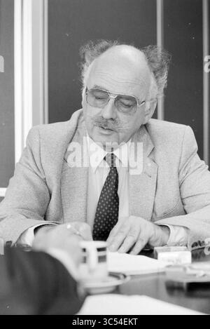 Herr Van Loon VNU Video Amsterdam, People, Video, VNU Association of Dutch Publishers, Amsterdam, Niederlande, 21.09.1981 Whizgle News, Dutch Desk, Niederlande, 1950-2000 Ein älterer Mann mit übergroßer Sonnenbrille und hellem Blazer sitzt an einem Tisch und konzentriert sich auf die Dokumente vor ihm. Er hat unverwechselbares, widerspenstiges Haar und einen nachdenklichen Ausdruck, der in eine ernsthafte Diskussion verwickelt erscheint. Eine Hand und eine Kaffeetasse sind im Vordergrund sichtbar, was auf eine gemeinsame Umgebung hindeutet. Stockfoto