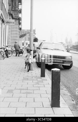 Geparkte Autos am Kai (der Spaarne?), 00-10-1989 Whizgle News, Dutch Desk, Niederlande, 1950-2000 Eine ruhige Straßenszene mit einem geparkten Auto auf einem Bürgersteig mit einem Fahrrad, das an einem Pfosten angelehnt ist. Im Hintergrund sieht man eine Person, die mit einem Fahrrad interagiert, während ein Gebäude mit einem Schild in der Nähe sichtbar ist. Stockfoto