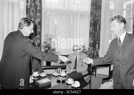 Ehren von 3 Schullehrern., Ehren, 23-06-1972 Whizgle News, Dutch Desk, Niederlande, 1950-2000 zwei Männer in Anzügen haben einen Handschlag, der ein bedeutendes Abkommen oder eine Partnerschaft symbolisiert. Ein dritter Mann sitzt in der Nähe und beobachtet die Interaktion, während ein Tisch mit Kaffeetassen und einem kleinen Dessert gedeckt ist. Die Einrichtung verfügt über große Fenster mit Vorhängen und Blumenarrangements, die eine formelle Atmosphäre vermitteln. Stockfoto