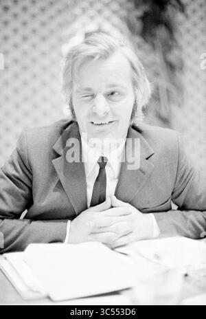 Beverwijk council Chefs, Beverwijk Municipal council, 27-01-1972 Whizgle News, Dutch Desk, Niederlande, 1950-2000 Ein Mann im Anzug sitzt mit verspieltem Ausdruck an einem Tisch, während er seine Hände übereinander legt. Seine Frisur und Kleidung deuten auf einen Stil aus der Mitte des 20. Jahrhunderts hin und verleihen der Szene einen nostalgischen Charme. Stockfoto