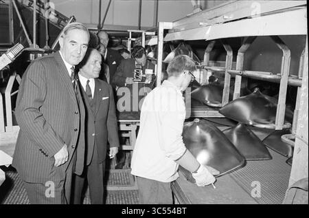 Präsident Bourgiba in unserem Land, königliche Empfänge und königliche Besuche, 06-07-1966 Whizgle News, Dutch Desk, Niederlande, 1950-2000 in einer Produktionsstätte wird Eine Gruppe von Männern beobachtet, wobei ein Mann im Anzug eine Arbeitsstation inspiziert, an der ein Arbeiter große, glänzende Metallgegenstände bearbeitet. Die Umgebung wirkt industriell, wobei verschiedene Werkzeuge und Geräte im Hintergrund sichtbar sind. Stockfoto