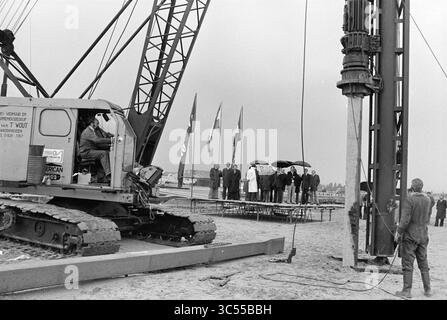 First Pile Bornholm, New District, H'dorp, First Pile, 05-10-1977 Whizgle News, Dutch Desk, Niederlande, 1950-2000 Auf Einer Baustelle befindet sich ein großer Kran, der einsatzbereit ist, während eine Gruppe von Zuschauern, teilweise mit Regenschirmen, auf einer Plattform in der Nähe steht und aufmerksam das Geschehen beobachtet. Flags bewegen sich im Hintergrund und fügen dem Ereignis Kontext hinzu. Stockfoto