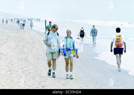 Beach 6 Days, 28-07-1998 Whizgle News, Dutch Desk, Niederlande, 1950-2000 Ein paar Spaziergänge entlang eines Sandstrandes und genießen die Gesellschaft des anderen, während sie Orangen halten. Andere gehen im Hintergrund vorbei und genießen die Atmosphäre am Meer. Die Wellen schlängeln sanft am Ufer und erzeugen eine entspannte Atmosphäre. Stockfoto