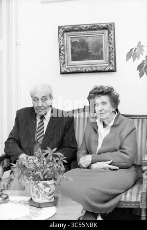 50-jähriges Baas-Bank-Paar, Paare, 31-10-1989, Whizgle News, Dutch Desk, Niederlande, 1950-2000 ein älteres Ehepaar sitzt nebeneinander auf einem gemusterten Sofa in formeller Kleidung. Der Mann trägt einen gestreiften Anzug mit Krawatte, während die Frau eine helle Bluse und einen Pullover trägt. Eine Topfpflanze liegt auf einem kleinen Tisch vor ihnen, und ein Gemälde hängt an der Wand dahinter. Ihre Ausdrucksformen vermitteln ein Gefühl von Wärme und Gemeinschaft. Stockfoto