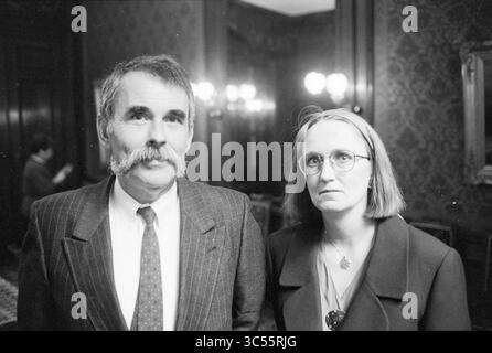 Porträt eines Mannes und einer Frau in einem Zimmer, 00-10-1992 Whizgle News, Dutch Desk, Niederlande, 1950-2000 Ein Mann mit einem hervorragenden Schnurrbart steht neben einer Frau mit Brille und glattem Haar, beide blicken direkt auf den Betrachter mit ernsten Ausdrücken. Der Hintergrund ist reich dekoriert und dezent beleuchtet, was auf eine elegante Umgebung hindeutet. Stockfoto
