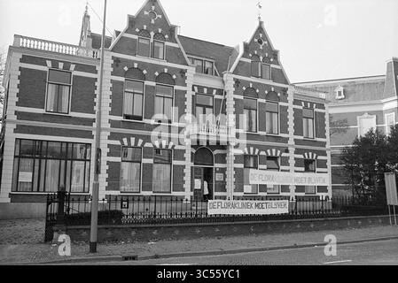 Erw. Flora Clinic, Exterior, 04.11-1973 Whizgle News, Dutch Desk, Niederlande, 1950-2000 Ein historisches Gebäude mit kunstvollen architektonischen Details und einer markanten Fassade mit einem Banner mit der Aufschrift „DE FLORALENKLINIE MOET BLIJVEN“, das eine Botschaft der Unterstützung oder des Protestes andeutet. In der Umgebung gibt es einen Zaun und einige Grünflächen. Stockfoto