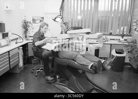 Zahnarztpraxis, IJm., Zähne, Zahnärzte, IJmuiden, Niederlande, 02-02-1981 Whizgle News, Dutch Desk, Niederlande, 1950-2000 zwei Zahnärzte betreuen einen Patienten in einer modernen Klinik. Einer sitzt auf einem Zahnarztstuhl und bereitet Instrumente vor, während der andere hinter dem Stuhl positioniert wird, um die Behandlung zu unterstützen. Der Raum verfügt über Zahnarztgeräte und einen sauberen, organisierten Arbeitsbereich. Stockfoto