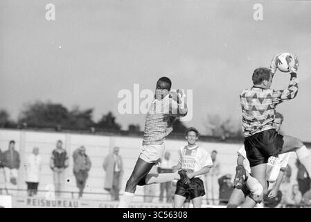 Football RCH - ADO'20, Heemstede, Niederlande, 06-10-1990 Whizgle News, Dutch Desk, Niederlande, 1950-2000 Ein Fußballspieler in der Mitte der Action bereitet sich darauf vor, den Ball zu schießen, während ein Torhüter springt, um ihn zu fangen. Andere Spieler und Zuschauer sind im Hintergrund zu sehen, was die Intensität der Szene erhöht. Stockfoto