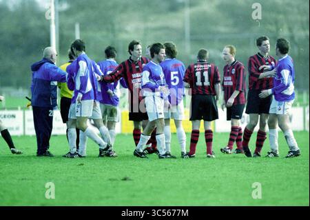 Fußball: Stormvogels - EDO, IJmuiden, IJmuiden, Niederlande, 07-02-2004 Whizgle News, Dutch Desk, Niederlande, 1950-2000 Ein hitziges Fußballspiel zeigt Spieler aus zwei Teams, die Handshakes austauschen und trotz der Wettkampfatmosphäre Kameradschaft zeigen. Die Szene fängt die Intensität des Sports ein, während Spieler in lebhaften Uniformen auf einem grasbewachsenen Feld nach dem Spiel interagieren. Stockfoto