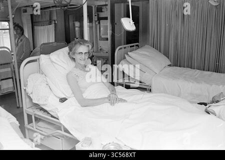 Krankenhausschiff Henri Dunant [J. Henry Dunant], Rotes Kreuz, Rotes Kreuz Krankenhaus, 01-09-1970 Whizgle News, Dutch Desk, Niederlande, 1950-2000 eine ältere Frau mit Brille lächelt, während sie in einem Krankenhausbett ruht, umgeben von einer beruhigenden Umgebung mit anderen unbewohnten Betten in der Nähe. Sie scheint sich wohl und wohl zu fühlen und vermittelt trotz der klinischen Umgebung ein Gefühl der Ruhe. Stockfoto