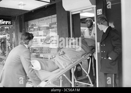 Raub des Juweliergeschäfts Labelle, Generaal Cronjéstraat 26, Haarlem, Generaal Cronjéstraat, Niederlande, 27-03-1979 Whizgle News, Dutch Desk, Niederlande, 1950-2000 Eine trage wird durch eine Tür gemanövriert, auf der eine Person mit einer Decke liegt. Zwei Personen helfen bei der Bahre, während eine dritte Person am Eingang steht und die Situation beobachtet. Im Hintergrund sind mehrere Fahrzeuge zu sehen. Stockfoto