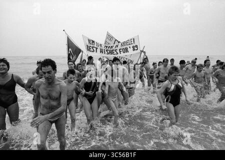 Neujahrstauchen Zandvoort, Neujahr, Zandvoort, 01-01-1989 Whizgle News, Dutch Desk, Niederlande, 1950-2000 Eine lebendige Gruppe von Menschen plätschert freudig durch die Meereswellen und feiert mit Bannern, die Botschaften der Hoffnung und der guten Wünsche für das kommende Jahr vermitteln. Ihre energiegeladene Präsenz fängt ein Gefühl von Gemeinschaft und sorglosem Geist ein. Stockfoto