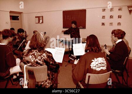 Mrs. Camphorst, Leiterin der Musikschule, 07-01-1997 Whizgle News, Dutch Desk, Niederlande, 1950-2000 Eine Gruppe von Musikern versammelt sich in einem Klassenzimmer und nimmt an einer Musikpraxis Teil, die von einem Dirigenten geleitet wird. Verschiedene Instrumente sind vorhanden, und Noten sind vor den Teilnehmern sichtbar, die fokussiert und in die kollaborative Atmosphäre eingebunden wirken. Stockfoto