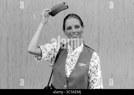 Stewardess Berkel Versteeg Transavia, 28-06-1992 Whizgle News, Dutch Desk, Niederlande, 1950-2000 Eine lächelnde Frau hält ein kleines Objekt über dem Kopf, gekleidet in einem lebhaften gemusterten Hemd und einer Weste, die ein fröhliches und einnehmendes Verhalten verkörpert. Sie scheint bereit zu sein, etwas Besonderes zu teilen. Stockfoto