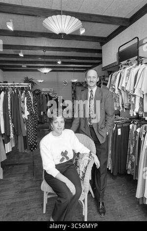 Modehaus Silhouette Bloemendaal + Besitzer, Mode, Bloemendaal, 29-03-1990 Whizgle News, Dutch Desk, Niederlande, 1950-2000 Ein gut gekleidetes Paar steht selbstbewusst in einem Bekleidungsgeschäft, umgeben von einer lebhaften Ausstellung von Kleidungsstücken, die an Regalen hängen. Die Frau sitzt bequem in einem Stuhl und trägt einen stylischen Pullover, während der Mann neben ihr steht und ein poliertes Auftreten ausstrahlt. Das Ladenambiente vermittelt eine einladende Atmosphäre für Käufer. Stockfoto