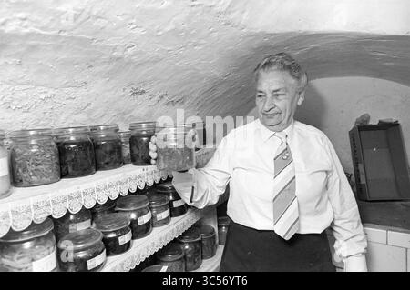 Witwe Kort im Haus Oud Velsen, Personen, Oud-Velsen, 24-05-1982 Whizgle News, Dutch Desk, Niederlande, 1950-2000 Eine Person, die ein Glas hält, steht in einem schwach beleuchteten Keller, der mit Regalen mit konservierten Lebensmitteln gesäumt ist, und zeigt eine Reihe von ordentlich angeordneten Gläsern, die mit verschiedenen Inhalten gefüllt sind. Die Atmosphäre vermittelt ein Gefühl von Nostalgie und Sorgfalt für die traditionelle Konservierung von Lebensmitteln. Stockfoto