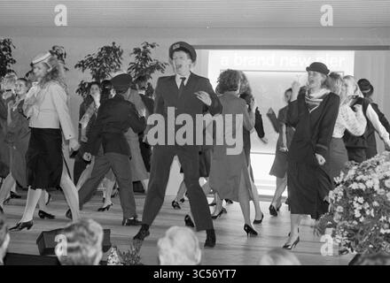 Eröffnung C-Pier Schiphol, Schiphol, 13-12-1987 Whizgle News, Dutch Desk, Niederlande, 1950-2000 Eine lebhafte Performance mit einer Gruppe von Tänzern in stilvoller Kleidung, die synchronisierte Bewegungen und Lächeln zeigen. Im Hintergrund befindet sich ein großer Bildschirm mit dem Text „ein brandneuer Pier“, der auf ein festliches Thema hinweist. Die Szene ist voller Energie und Begeisterung, mit einem Schwerpunkt auf Mode und Choreographie. Stockfoto