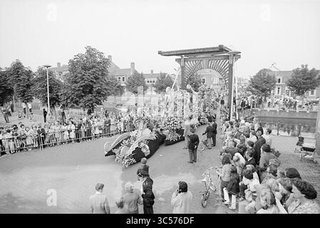 Blumenparade Aalsmeer, Blumenparade, Blumenausstellung, 04-09-1971 Whizgle News, Dutch Desk, Niederlande, 1950-2000 Eine lebhafte Paradeszene mit einem reich verzierten Wagen mit Blumenschmuck entfaltet sich, während sich hinter Barrieren eine Menschenmenge versammelt, die die Festlichkeiten sehnt. Bäume säumen die Straße, und ein großes Bauwerk im Hintergrund umrahmt die Prozession und verleiht der Veranstaltung eine festliche Atmosphäre. Menschen jeden Alters, einige auf Fahrrädern, sind an der Feier beteiligt. Stockfoto