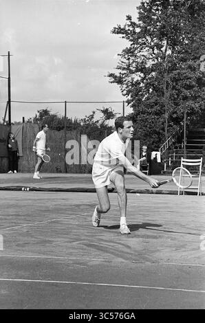 Tennis Brederode III, Jaidip Mukerjea-Tom Okker, Santpoort, 197-07-1965 Whizgle News, Dutch Desk, 30 Niederlande, 1950-2000 zwei Tennisspieler spielen auf einem von Bäumen umgebenen Spielfeld ein Spiel. Ein Spieler springt vorwärts, um den Ball mit konzentrierter Entschlossenheit zu treffen, während der andere im Hintergrund steht und bereit ist zu reagieren. Zuschauer können das Spiel von der Seitenlinie aus beobachten. Stockfoto