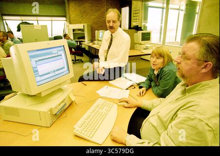 Frans van Bremen, Telegraaf, Amsterdam, Niederlande, 25-10-2000 Whizgle News, Dutch Desk, Niederlande, 1950-2000 Eine Gruppe von drei Fachleuten arbeitet an einem Schreibtisch zusammen und konzentriert sich auf einen Computerbildschirm, der eine Softwareschnittstelle anzeigt. Eine Person im Anzug beobachtet nachdenklich, während die anderen beiden in lässiger Kleidung aktiv an Diskussionen teilnehmen, umgeben von zusätzlichen Computern und Bürogeräten. Stockfoto