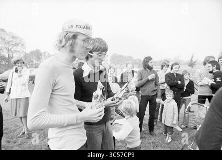 Radrennen Damiate Preis Spaarndam, Haarlems Dagblad etc. Und IJmuider Courant and Koeri, Cycling, 2009-09-1976 Whizgle News, Dutch Desk, Niederlande, 30 1950-2000 Eine Gruppe von Personen versammelte sich im Freien, wobei zwei Personen im Vordergrund gepackte Gegenstände hielten. Die Menge scheint in Unterhaltung und Lachen verwickelt zu sein, während Kinder spielen und Erwachsene im Hintergrund Erfrischungen genießen. Bäume und ein Fahrzeug sind beiläufig sichtbar, was auf ein entspanntes gesellschaftliches Ereignis hindeutet. Stockfoto