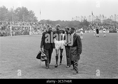 VSV - SHS, Football, 24-09-1961 Whizgle News, Dutch Desk, Niederlande, 1950-2000 Auf Einem überfüllten Sportplatz wird eine betroffene Szene gezeigt, in der ein Fußballspieler, der sichtbar verletzt ist, von zwei Männern unterstützt wird, während ein dritter in der Nähe steht und eine Tasche hält. Die Zuschauer im Hintergrund sehen aufmerksam zu und unterstreichen die Schwere der Situation. Stockfoto