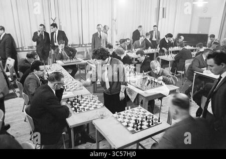 Five Ladies from Hoogoven Chess Tournament - Leser IJmuider Courant, Chess, 22-01-1965 Whizgle News, Dutch Desk, Niederlande, 1950-2000 Ein lebhaftes Schachturnier findet in einem geräumigen Raum statt, in dem zahlreiche Tische aufgestellt sind, von denen jeder von fokussierten Spielern besetzt ist, die tief nachdenklich sind. Einige Teilnehmer sind in intensiven Matches engagiert, während andere aufmerksam beobachten. Die Atmosphäre ist voller Konzentration, während die Köpfe über das klassische Spiel strategisch entscheiden. Stockfoto