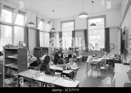 Schools Haarlem: Aufnahmen für Schulberatung Zeitung, Schools, Haarlem, Niederlande, 01-07-1981 Whizgle News, Dutch Desk, Niederlande, 1950-2000 Eine lebendige Klassenszene voller Schüler, die an verschiedenen Aktivitäten teilnehmen, wobei einige an Tischen arbeiten, während andere sich in einem zentralen Bereich versammeln. Sonnenlicht strömt durch große Fenster hinein und beleuchtet den Raum mit lehrreichen Materialien und Büchern. Die Atmosphäre spiegelt den Schwerpunkt auf Lernen und Zusammenarbeit wider. Stockfoto