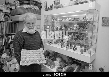 Ostereier bei Mr. Van de Poll, Palm Sunday and Easter Customs, 23-02-1988 Whizgle News, Dutch Desk, Niederlande, 1950-2000 ein älterer Mann hält stolz ein Tablett mit bunten Eiern und steht neben einer Vitrine mit einer beeindruckenden Auswahl an kunstvoll verzierten, eiförmigen Ornamenten. Die Regale im Hintergrund sind mit verschiedenen Gegenständen gesäumt, was die eklektische Atmosphäre des Raumes unterstreicht. Stockfoto