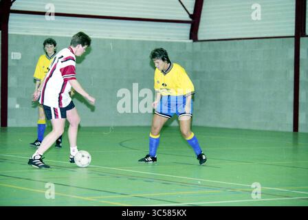 Trijn Reker, Hillegom, 23-11-2000 Whizgle News, Dutch Desk, Niederlande, 1950-2000 Bei Einem Wettkampf-Hallenfußballspiel spielt ein Spieler in einem gelben Trikot den Ball, während ein Gegner in einem rot-weißen Trikot den Ball genau verteidigt. Die farbenfrohen Uniformen heben sich vom grünen Hallenfeld ab und betonen den Fokus und das Können der Spieler im Spiel. Stockfoto