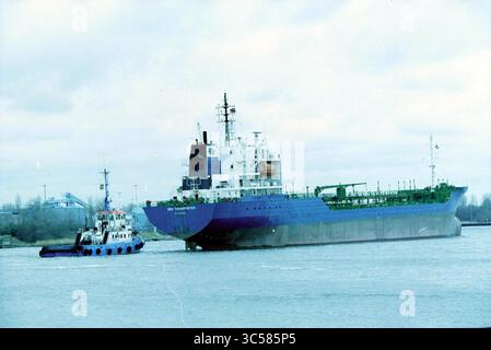 Terrasse Pontplein, IJmuiden, IJmuiden, Pontplein, Niederlande, 04-02-2002 Whizgle News, Dutch Desk, Niederlande, 1950-2000 Ein großes Frachtschiff navigiert durch ruhige Gewässer, unterstützt von einem kleineren Schlepper, der sich auf dem Weg zum Hafen befindet. Die Industriestrukturen sind im Hintergrund zu sehen, was auf einen aktiven Schifffahrtsbereich hindeutet. Stockfoto