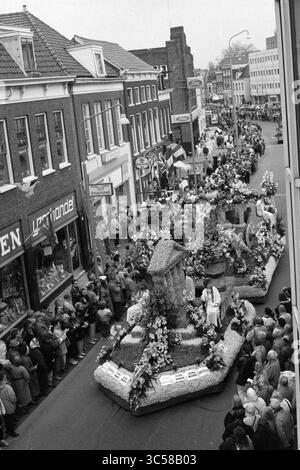 Flower Parade Haarlem - Hillegom, 22-04-1989 Whizgle News, Dutch Desk, Niederlande, 1950-2000 Eine lebhafte Parade schlängelt sich durch eine belebte Straße, die mit kunstvollen, mit Blumen bedeckten Wagen geschmückt ist. Die Zuschauer säumen die Seiten und beobachten die Festlichkeiten vor dem Hintergrund bezaubernder Gebäude und Ladenfronten. Farbenfrohe Fahnen und Dekorationen sorgen für die lebhafte Atmosphäre dieser Blumenfeier. Stockfoto