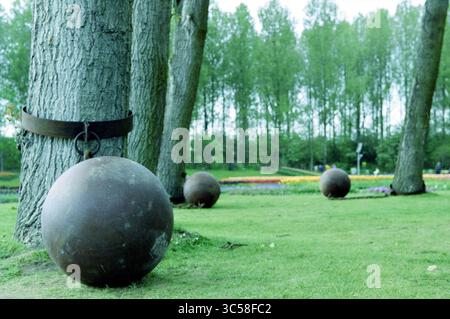Tulpen bei Floriade Vijfhuizen, Vijfhuizen, 02-05-2002 Whizgle News, Dutch Desk, Niederlande, 1950-2000 Eine große Metallkugel ist mit einem schweren Band sicher an einem Baum befestigt, während zusätzliche Kugeln über einen grasbewachsenen Bereich verteilt sind, umgeben von lebhaftem Grün. Stockfoto