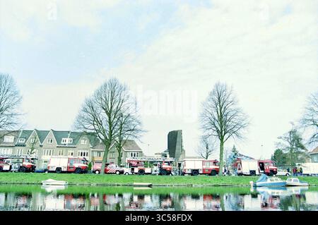 Gedenkfeier von 3 freiwilligen Feuerwehrleuten beim Koningkerk Fire, Haarlem, Kloppersingel 57, Niederlande, 24-03-2003 Whizgle News, Dutch Desk, Niederlande, 1950-2000 Eine Reihe von Feuerwehrfahrzeugen parkt entlang einer von Bäumen gesäumten Uferpromenade mit einer Kulisse von Häusern und einem hohen Gebäude, das teilweise in der Ferne sichtbar ist. Mehrere kleine Boote liegen in der Nähe vor, was die ruhige Szene noch verstärkt. Stockfoto