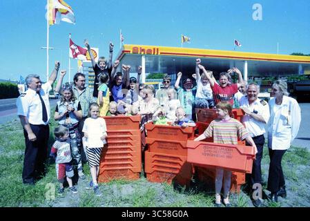 Verkauf von orangen Fischboxen, IJmuiden, Niederlande, 02-06-1997 Whizgle News, Dutch Desk, Niederlande, 1950-2000 Eine temperamentvolle Gruppe von Individuen, darunter Erwachsene und Kinder, versammelt sich um leuchtende rote Kisten, die mit erhobenen Fäusten zu feiern. Im Hintergrund befindet sich eine Tankstelle mit farbenfrohen Flaggen, die auf einen festlichen Anlass oder eine Veranstaltung hinweisen. Stockfoto