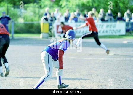 Softball: Terrasvogels - Onze Gezellen, Santpoort, Santpoort, 28-06-2002 Whizgle News, Dutch Desk, Niederlande, 1950-2000 Ein junger Spieler, der ein blaues Trikot und Helm trägt, hockt sich auf dem Spielfeld, während ein roter Batter auf dem Spielfeld schwingt, während die Zuschauer im Hintergrund zuschauen. Stockfoto